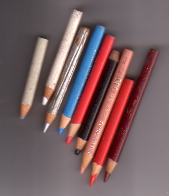 Nine well-used colored pencils and pastels fanned out on grey — silvers, blues, reds, black and brown