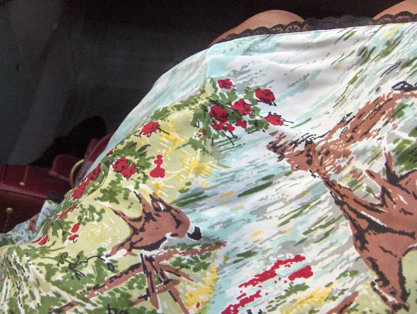 Looking down at a new dress printed with deer, trees and red flowers — a Bambi-esque forest scene with black lace at the neckline