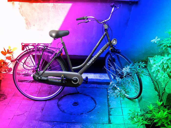 A black Oxford city bicycle against a wall, the whole photo washed in rainbow gradients from red through magenta to green A black Oxford city bicycle against a wall, the whole photo washed in rainbow gradients from red through magenta to green