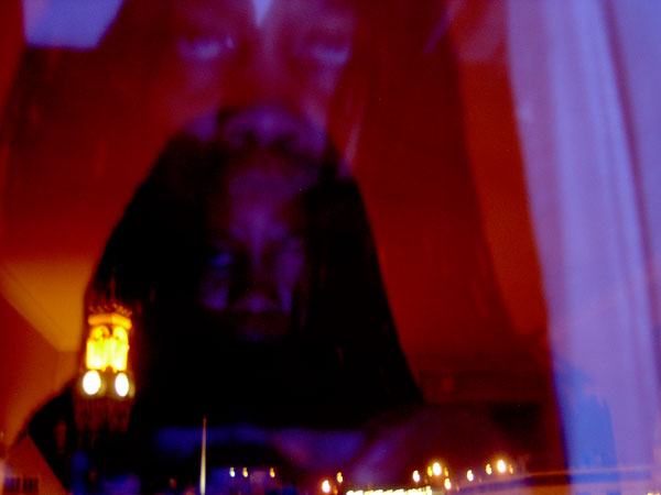 Double exposure in reds and blues: a sleeping dark face overlaid with a lit clock tower and a night street's lights