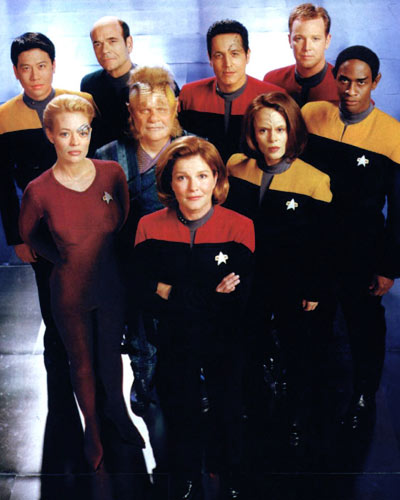Star Trek Voyager cast photo: Janeway front and center with arms crossed, the crew in red and gold uniforms around her