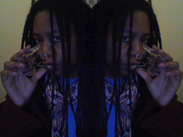 Mirrored webcam self-portrait: face doubled down the center line, drinking from a glass, dreadlocks framing both halves
