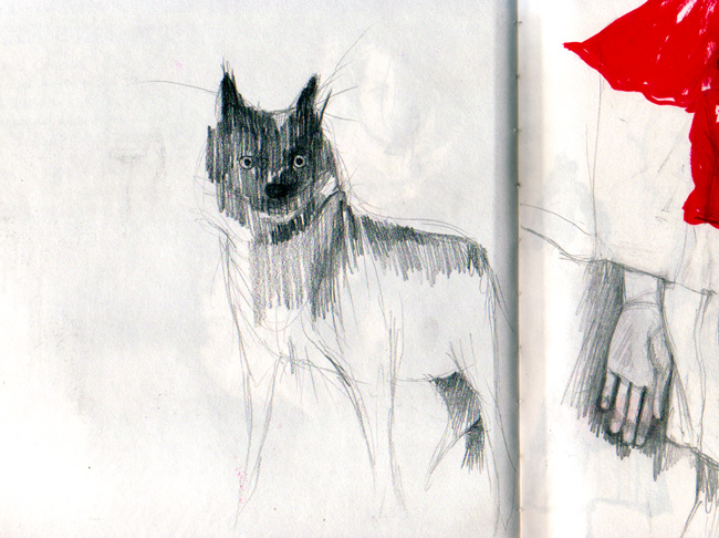 Sketchbook spread: pencil study of a shaggy black-and-white wolf standing guard, a red-hooded shape and a small drawn hand on the facing page