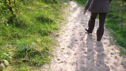 Walking behind someone on a sandy path between grassy dunes, cigarette in hand, long shadows