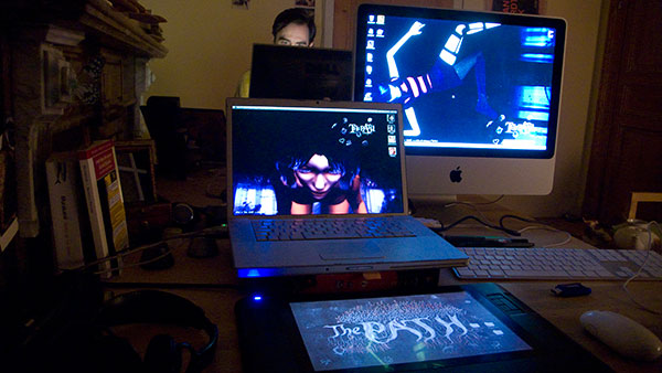 Night desk: laptop and iMac both showing The Path (Ruby leaning in headlights, a striped-sock scene), the logo glowing on a Wacom below, Michael behind the far monitor Night desk: laptop and iMac both showing The Path (Ruby leaning in headlights, a striped-sock scene), the logo glowing on a Wacom below, Michael behind the far monitor