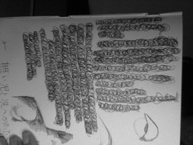 Sketchbook page filled with dense spiral scribble columns, a small eye and profile drawn below, Japanese writing in the margin