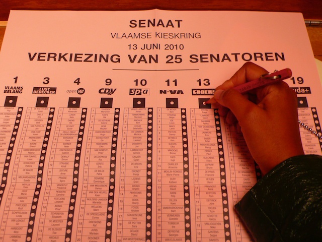 Belgian Senate ballot, 13 June 2010, pink paper listing 25 senators by party column; a hand with a pencil hovers over Groen!