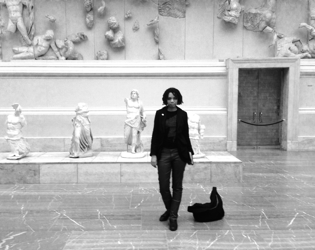 Standing small before the Pergamon Altar friezes in Berlin, hands at sides, bag dropped on the marble floor, battling gods overhead