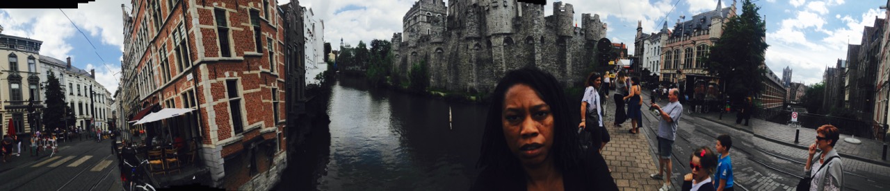 Panorama on the Gravensteen bridge in Ghent, unimpressed face in the foreground, the castle and canal curving behind, tourists at the rail