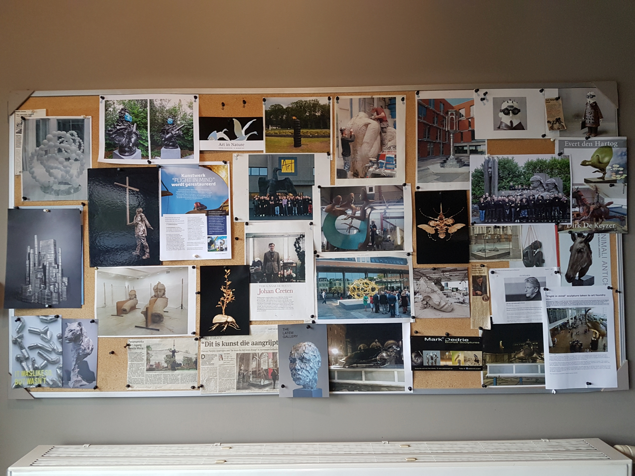 Studio corkboard packed with sculpture clippings: bronze foundry photos, Johan Creten and Dirk De Keyzer pages, insects, casts, a blue clay head, 'IT WAS LIKE SO BUT WASN'T'