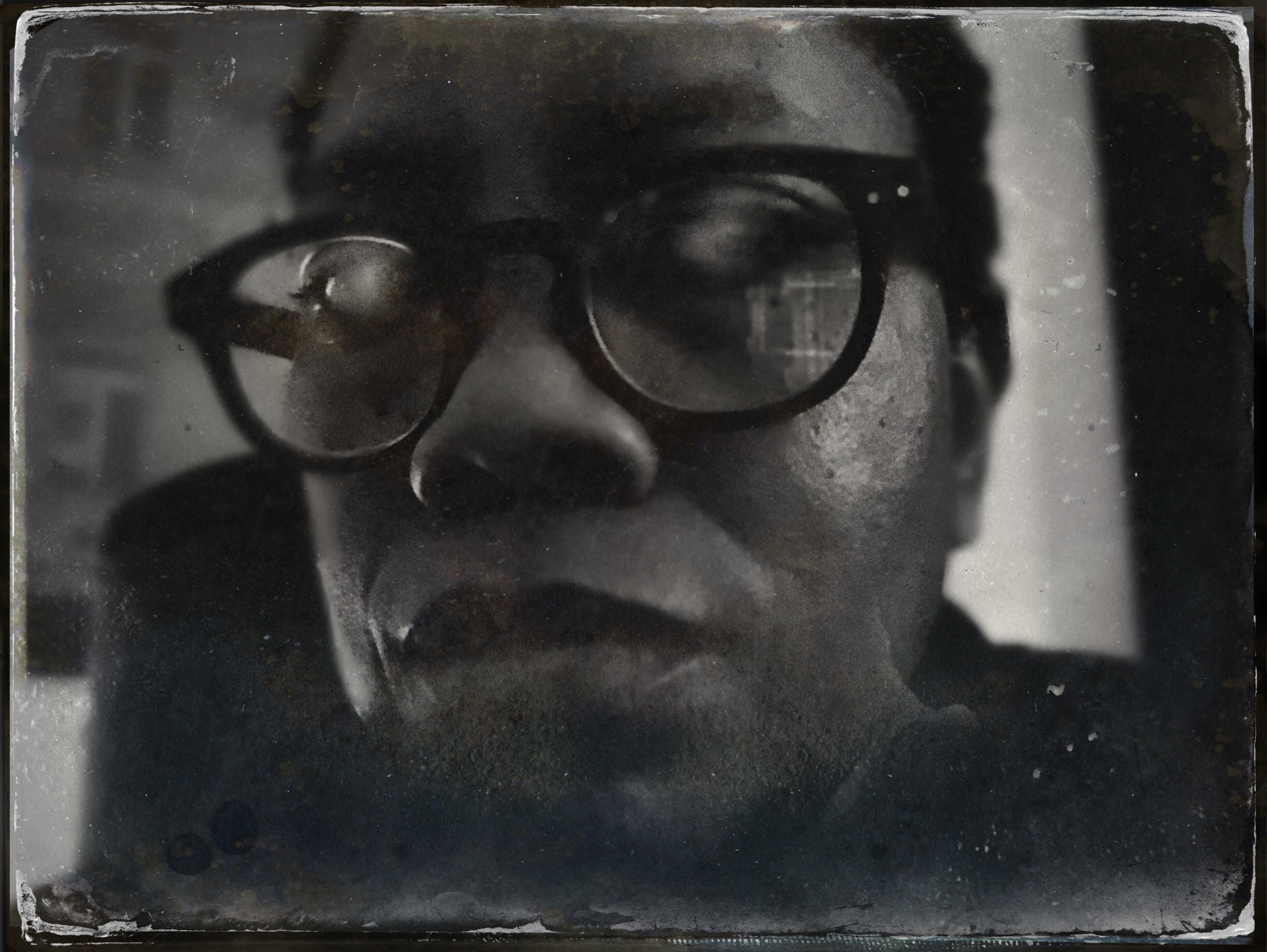 Tintype-style self-portrait, very close: round dark-rimmed glasses, window light on one side, the plate scratched and spotted Tintype-style self-portrait, very close: round dark-rimmed glasses, window light on one side, the plate scratched and spotted