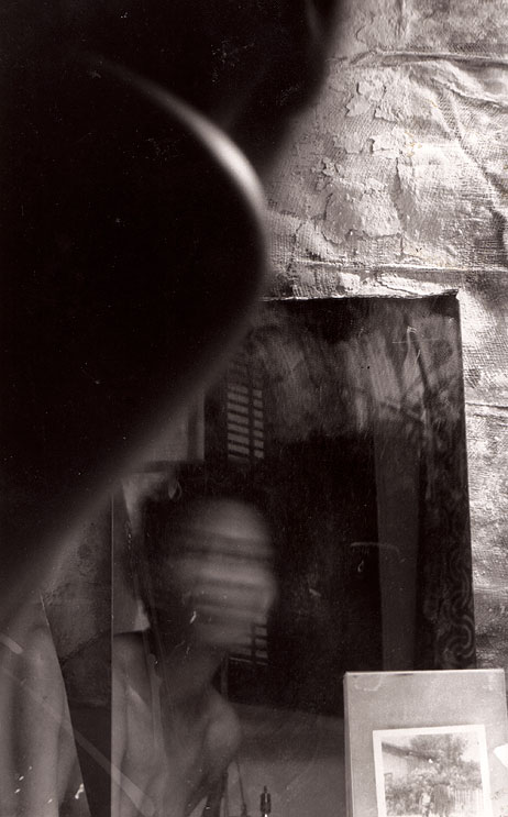 Black-and-white double exposure on 2nd Street: a blurred face streaked with motion in a mirror, plaster wall and shuttered window folding into shadow