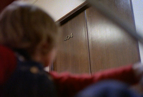 Film still: a small blond child reaches up toward a brown hotel door numbered 404 — page not found