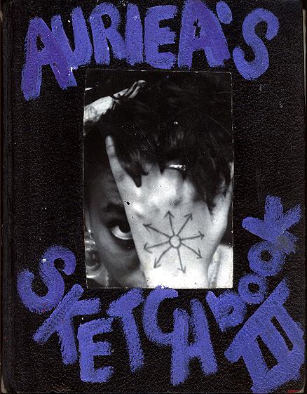 Cover of sketchbook 3: black leather painted 'AURIEA'S SKETCHBOOK III' in purple around a photo of a hand with a chaos-star drawn on it, one eye peering past