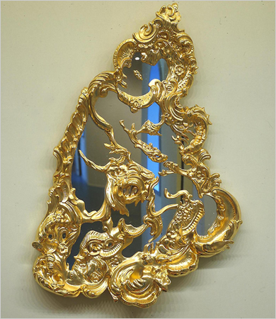 Gilded rococo openwork relief titled Christ and the Lamb: asymmetrical gold scrolls and foliage swirl over shaped mirror glass, the figures hidden in the ornament
