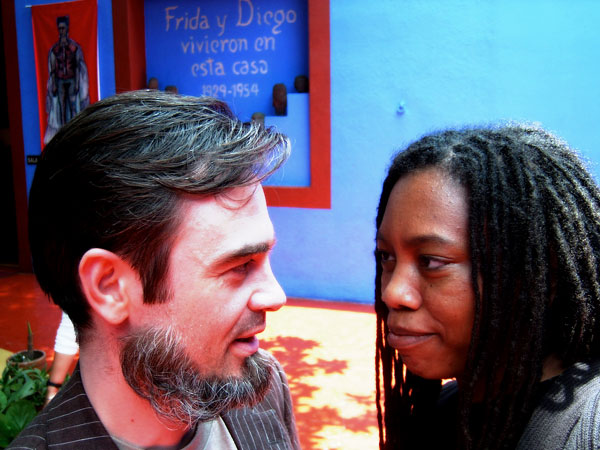 Auriea and Michaël in profile, nearly nose to nose in the blue courtyard of the Casa Azul under the words 'Frida y Diego vivieron en esta casa 1929–1954'