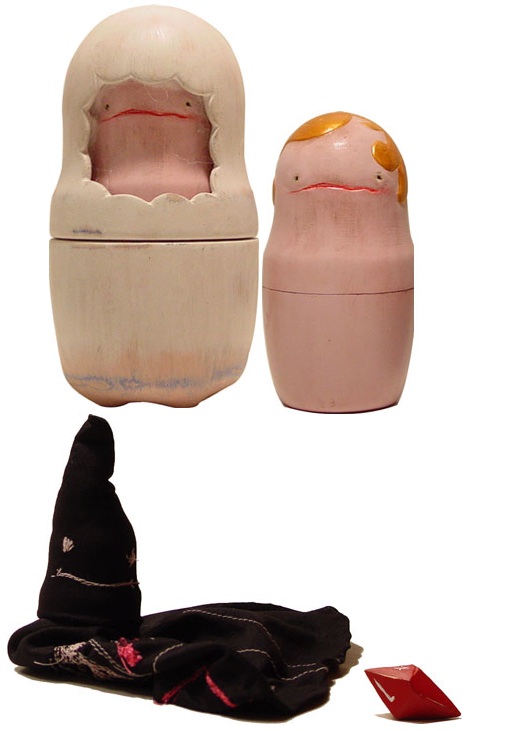 Two hand-painted matryoshka-style dolls with sad pink faces — one hooded in cream, one with a golden bob — above a black pointed hood and a tiny red gem Two hand-painted matryoshka-style dolls with sad pink faces — one hooded in cream, one with a golden bob — above a black pointed hood and a tiny red gem