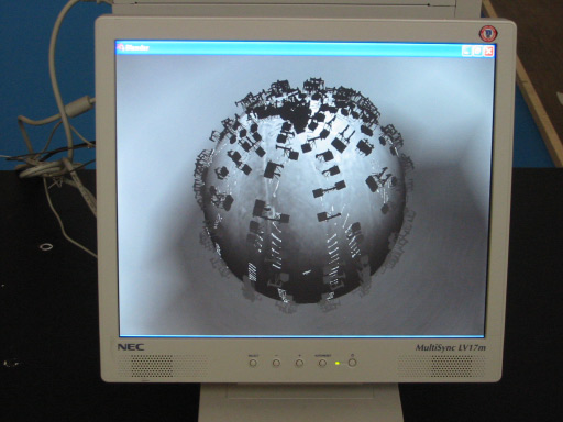An NEC monitor displaying a grey 3D sphere studded all over with fragments of buildings and figures, like a small ruined planet