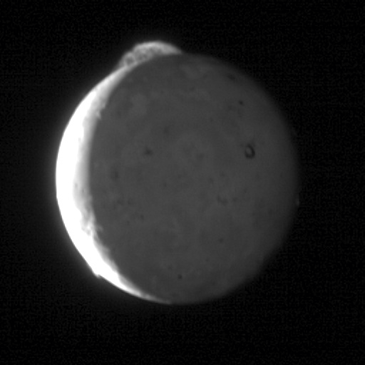 Spacecraft photograph of Jupiter's moon Io half in shadow, a volcanic plume erupting in a bright arc off its upper limb