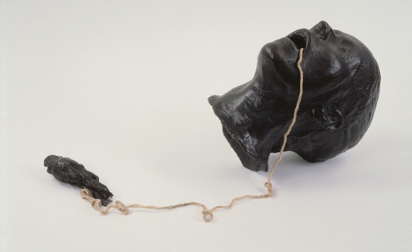 Kiki Smith's Getting the Bird Out: a black cast head lying cheek-down, a twine cord running from its mouth to a small black bird lying at its end