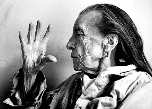 Black-and-white profile portrait of Louise Bourgeois in old age, eyes closed, holding up her long-fingered hand like a fan before her face