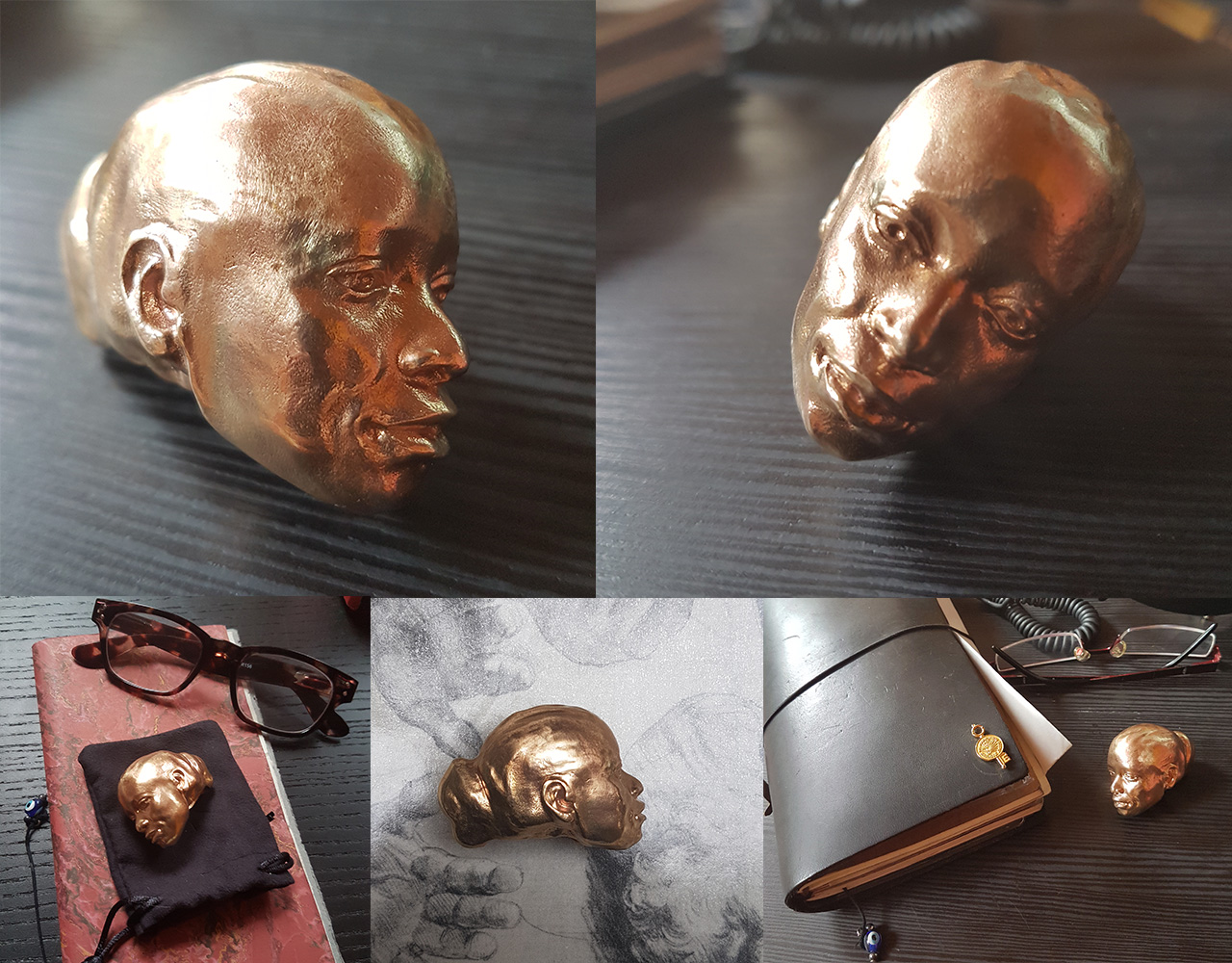 Five views of Object 01: a small polished bronze head of Auriea, bald with serene features, shown in the hand, on a black pouch, and beside a leather notebook