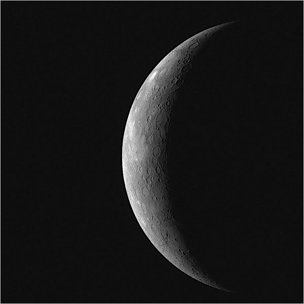 The planet Mercury as a thin grey crescent against black space, its cratered limb lit along the right edge