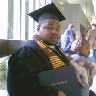 Tiny snapshot of Quinton at graduation, smiling in black cap and gown and holding a diploma
