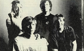 Small grainy black-and-white photo of Sonic Youth: Kim Gordon, Thurston Moore, Lee Ranaldo, and Steve Shelley posed against a dark wall