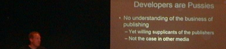 Blurry conference photo of a speaker beside a slide headed Developers are Pussies, arguing developers misunderstand the business of publishing