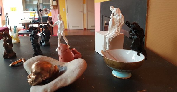 The studio worktable in 2017: a bronze head resting in a stone dish, a white David figurine, dark wax figures, a porcelain Venus on a box, and a teacup of tools