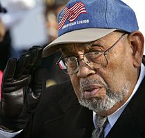 William Henry Harvey, in glasses and an American Legion cap stitched with United States flags, raises a leather-gloved hand to its brim