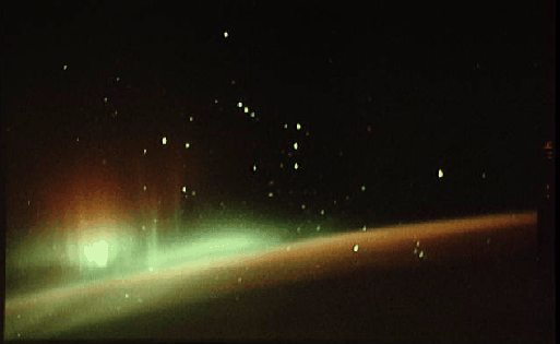 Photograph of stars scattered above a glowing green horizon band, a bright flare burning at the left edge