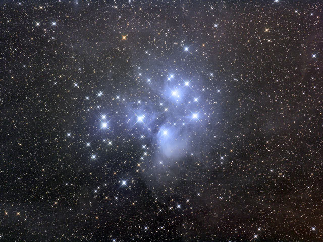 The Pleiades star cluster: the seven sisters blazing blue-white inside wisps of reflection nebula on a dense starfield