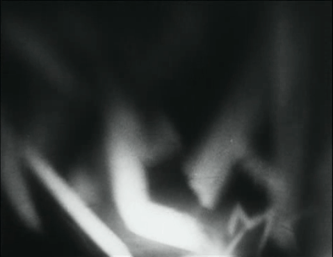 Blurred black-and-white frame: pale hands and limbs smeared in motion against darkness