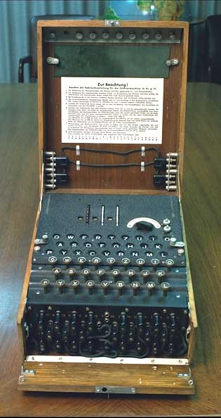 A German Enigma cipher machine open in its wooden case: lamp board, keyboard, plugboard, and the instruction plate Zur Beachtung in the lid