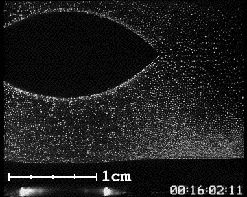 Black-and-white particle image: an eye-shaped void opening in a field of bright specks, with a 1 cm scale bar and timecode