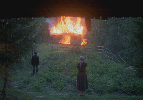 Film still: a man and a woman stand in a wet green garden watching a wooden barn burn, from Tarkovsky's Mirror