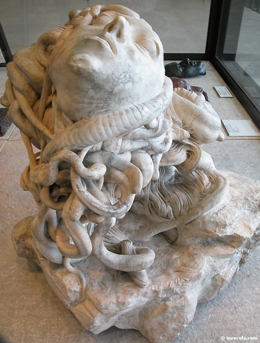 Colossal marble head of Medusa asleep on a rock, her face tipped back, wrapped in a mane of thick coiling snakes