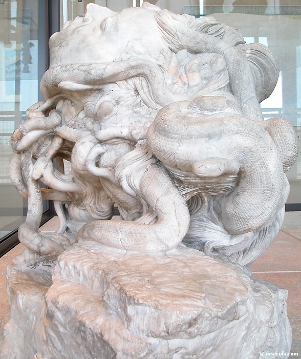The colossal marble Medusa from behind: heavy braids of snakes wind over the sleeping head, one serpent knotted around the mass