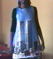 Grainy video still: a figure in a homemade paper dress printed with the two towers of the World Trade Center