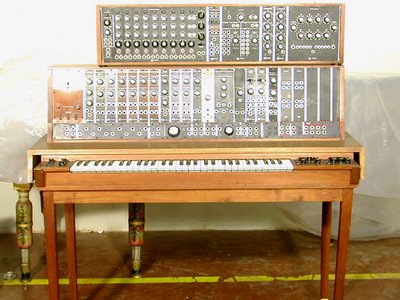 A modular synthesizer built into wooden cases on slender antique legs: two tiers of patch panels and dials above a keyboard