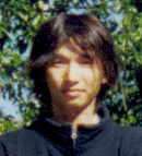 Snapshot portrait of game designer Fumito Ueda, dark hair falling across his face, against sunlit foliage